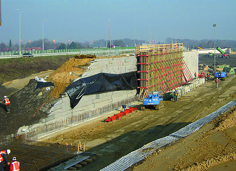 Baustelle mit mehreren Arbeitern und verschiedenen Maschinen bei der Erddruckentlastung und der Brückenwiderlagerung.