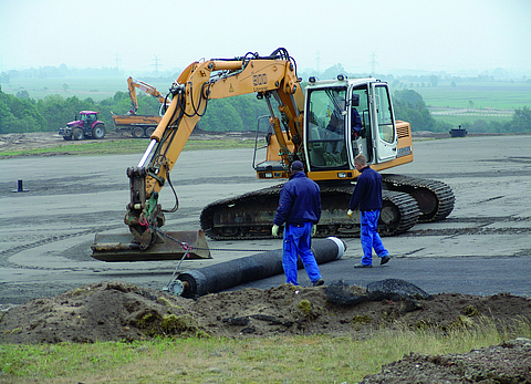 Bagger und Arbeiter beim Auslegen von Geosynthetischen Tondichtungsbahnen