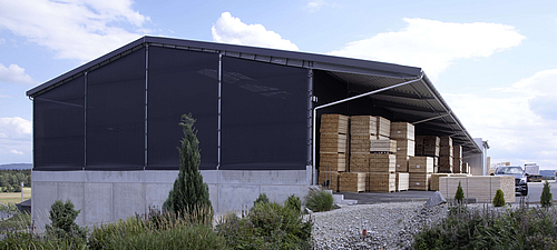 Tectura Fassadenverkleidung Lagerhalle mit textiler Fassade. Im Hintergund ein See mit bepflanztem Ufer